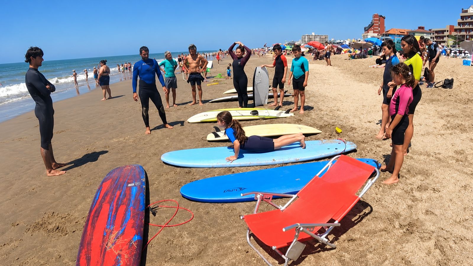 Clase de surf en la arena, con chicos y grandes practicando sobre las tablas
